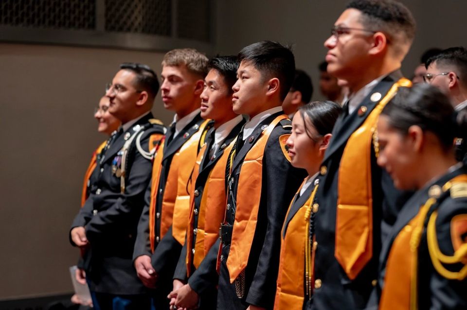 Cadetes em uniforme de gala com faixas laranja de honra em cerimônia acadêmica