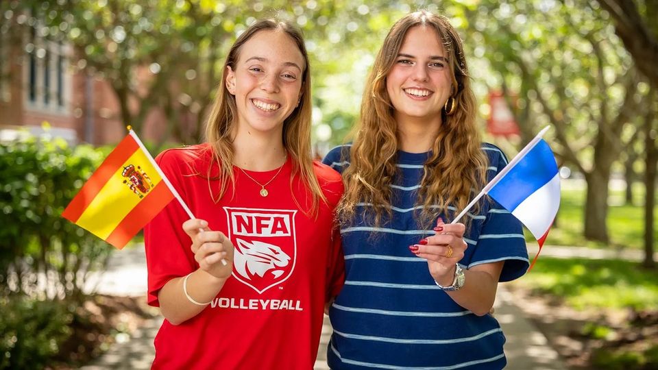 Dois alunos com camisetas de vôlei da NFA segurando bandeiras da Espanha e da Finlândia