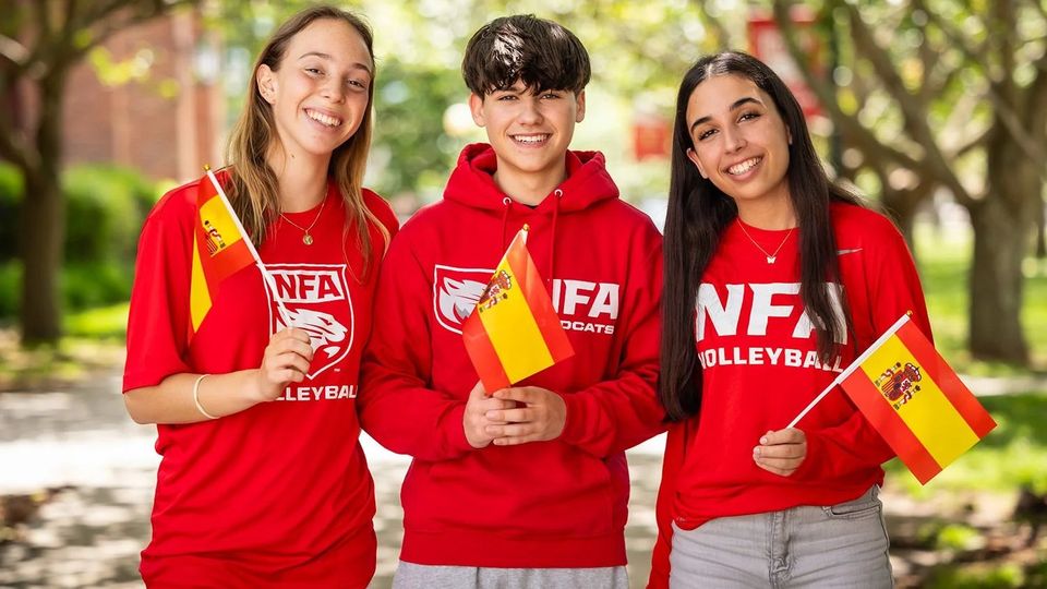 Três alunos com camisetas vermelhas da NFA com bandeiras da Espanha e da China