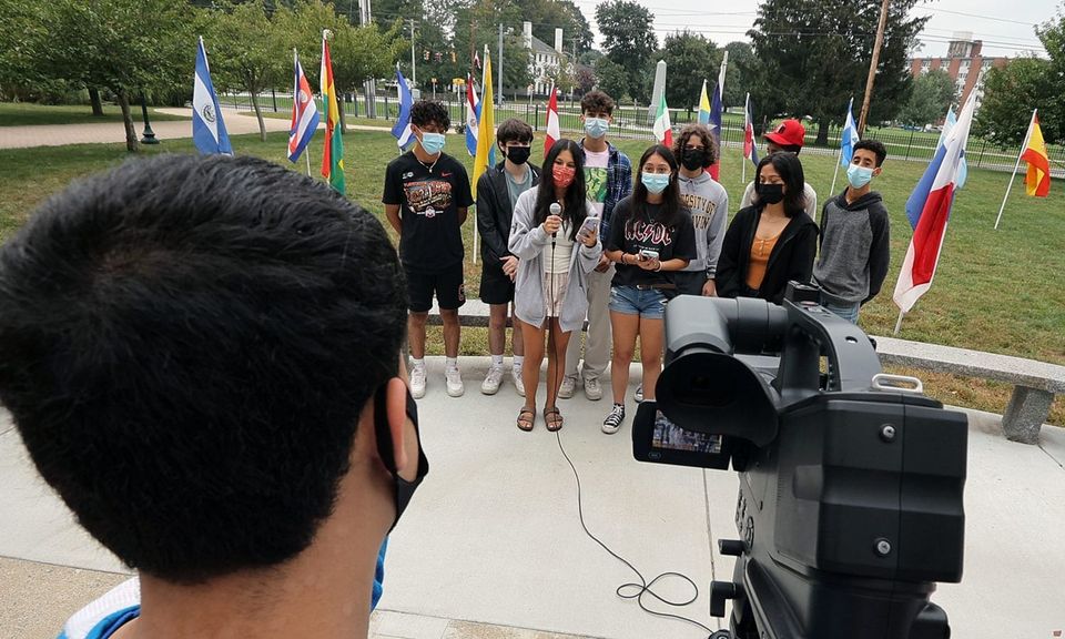 Alunos enfileirados atrás de bandeiras nacionais sendo filmados para a NFA TV