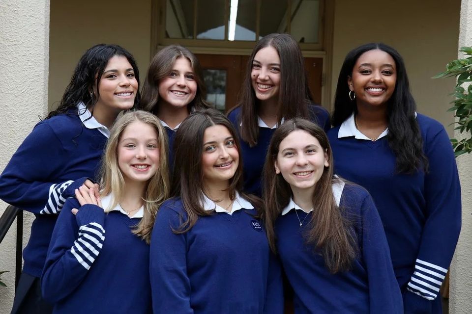 Grupo de alunas com suéteres azul-marinho do uniforme sorrindo juntas