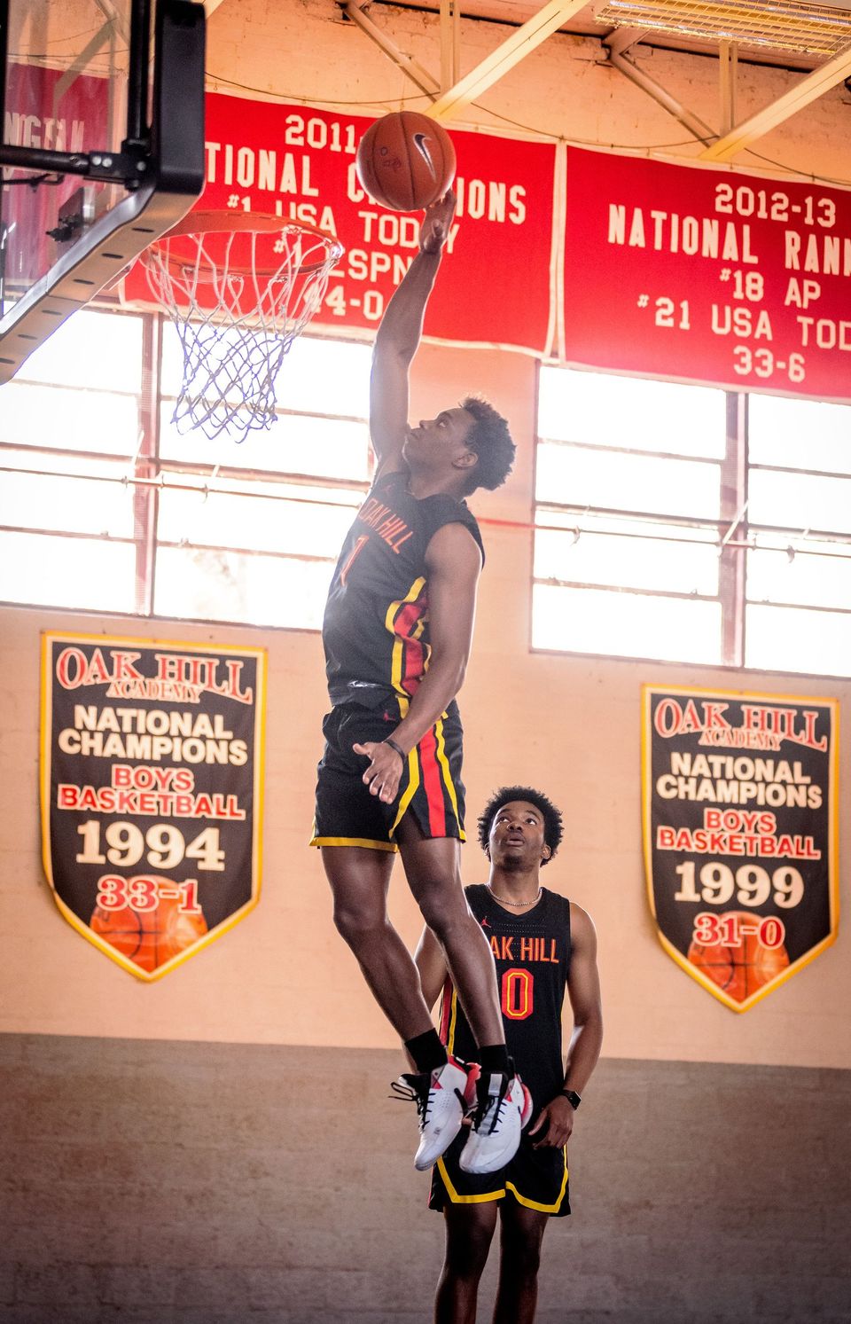 Jogador de basquete da Oak Hill enterrando no ginásio, sob as faixas de campeonatos nacionais