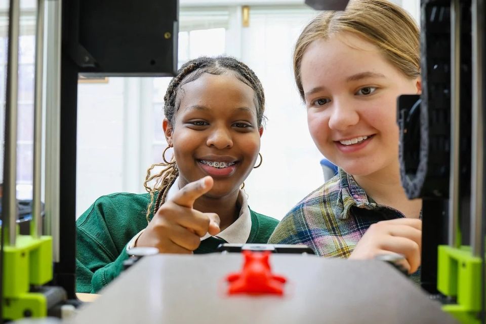 Duas alunas observando uma impressora 3D em aula