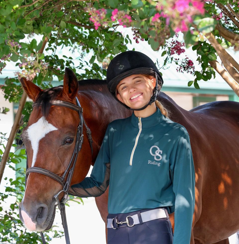 Aluna com traje de equitação ao lado de um cavalo no estábulo do campus