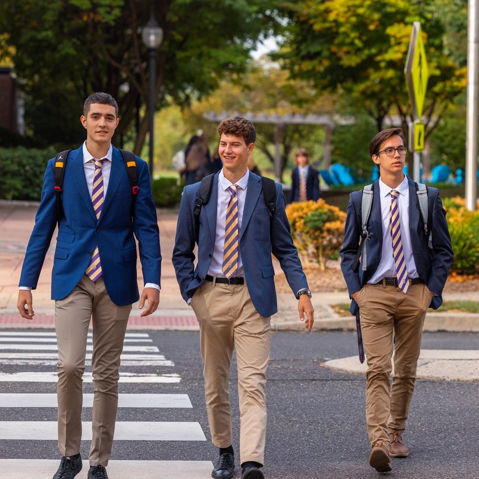 Três meninos de blazer azul-marinho atravessando a rua no dia de traje formal de segunda-feira