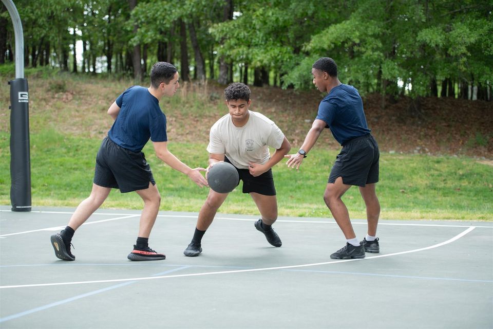 Três cadetes jogando basquete em quadra ao ar livre