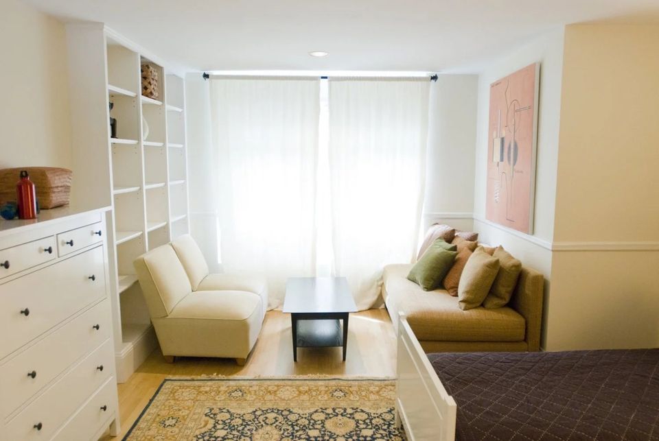 Sala de estar clara de uma casa de internato, com sofá, estantes e tapete