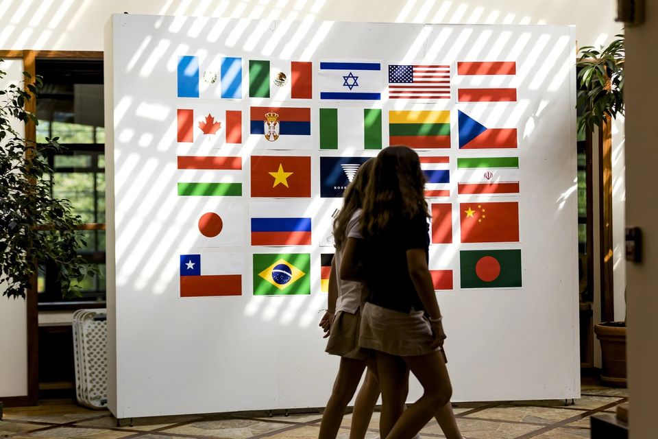 Alunas passando diante de um painel com bandeiras de vários países, incluindo a do Brasil