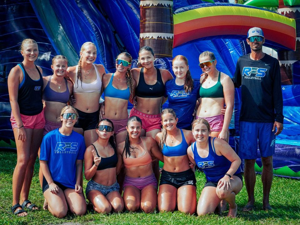 Meninas do vôlei da RPS e a técnica, molhadas e sorrindo, diante de um tobogã inflável em evento no campus