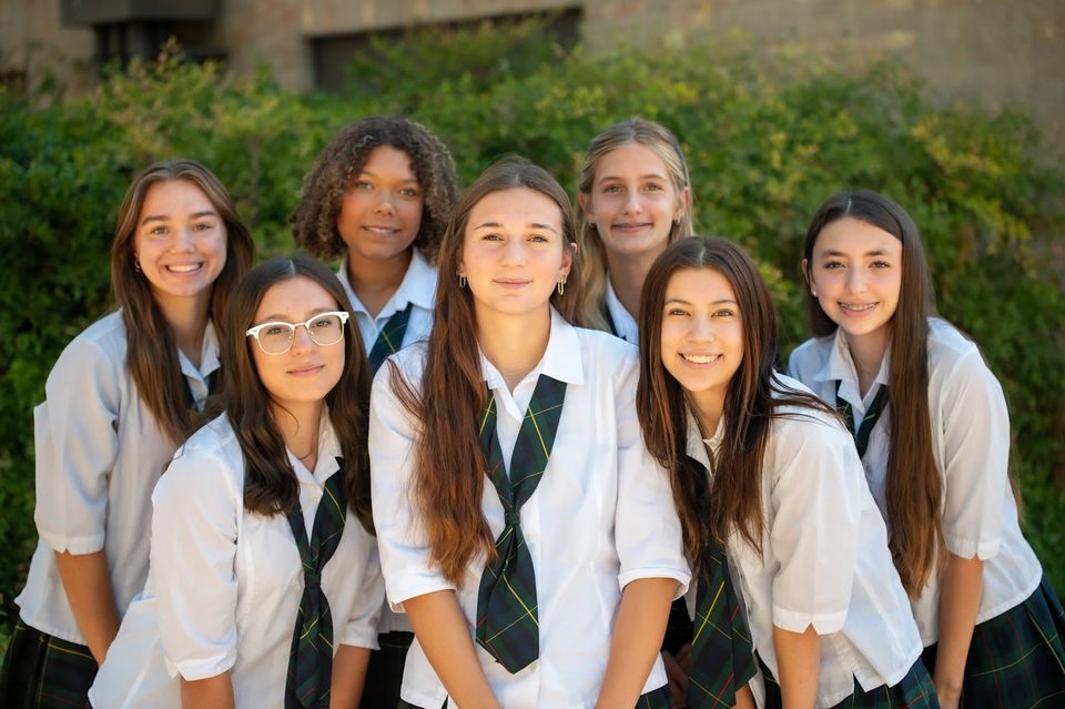 Grupo de sete alunas do ensino médio de uniforme da SMA com gravatas xadrez ao ar livre