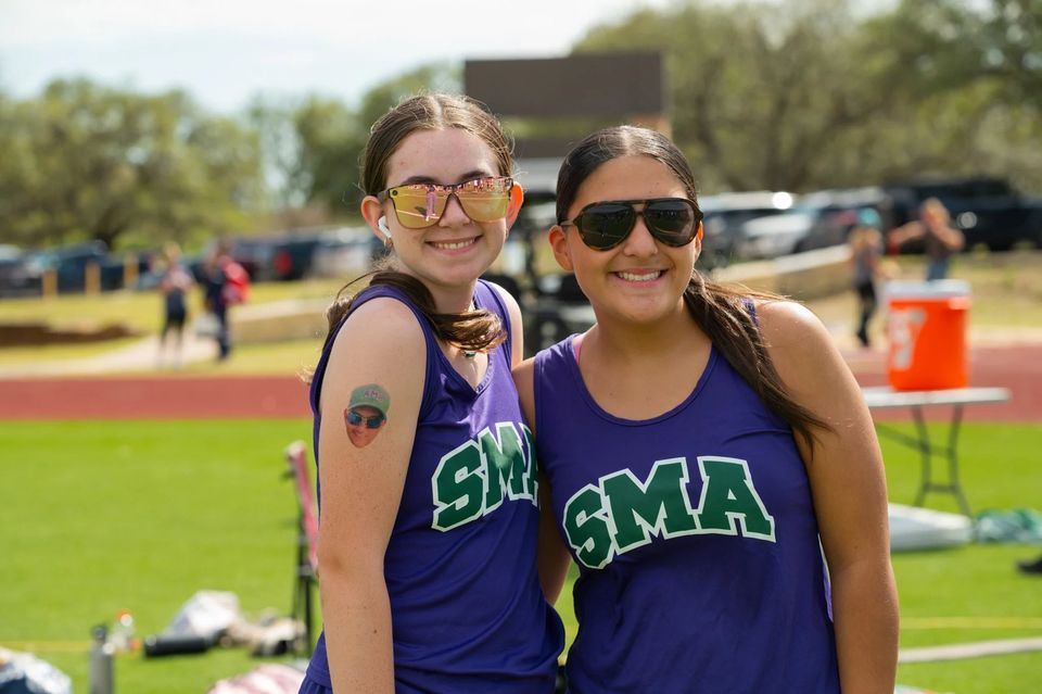 Dois atletas de atletismo da SMA de regata roxa sorrindo à beira da pista