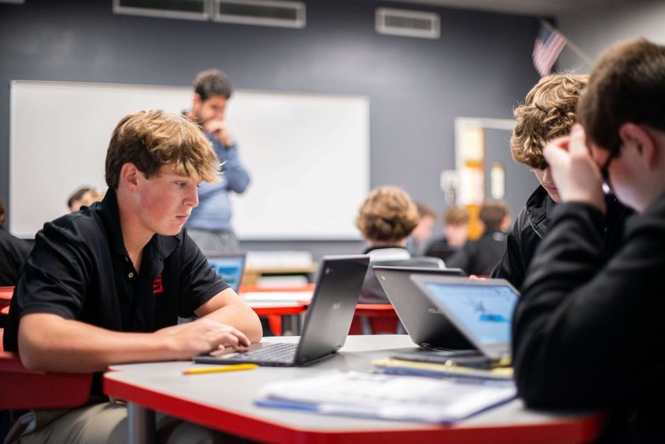 Alunos trabalhando em laptops em uma sala de aula do ensino médio
