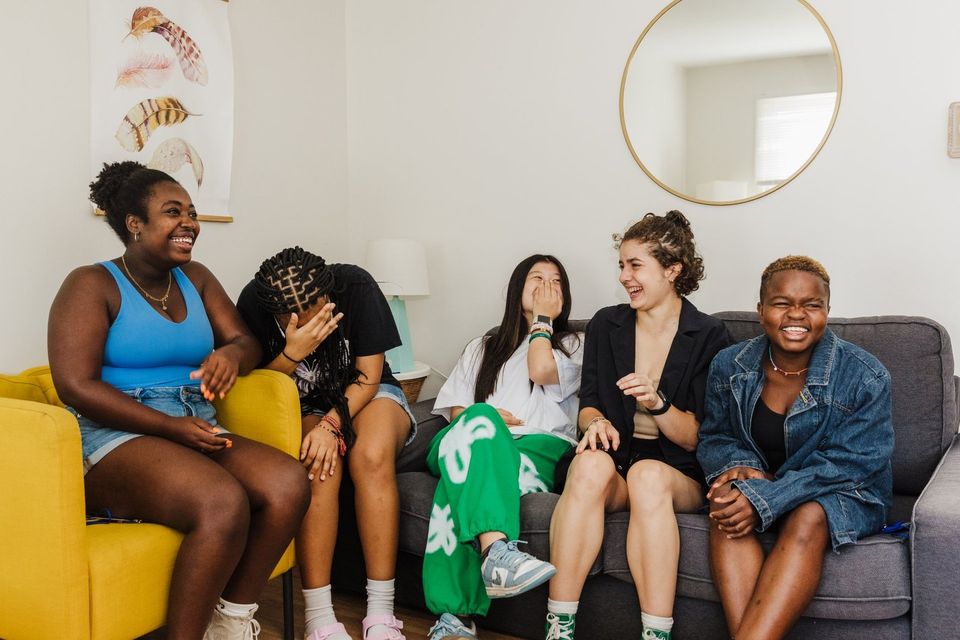 Grupo de alunas rindo juntas em sofás na sala comum do alojamento no dia da mudança