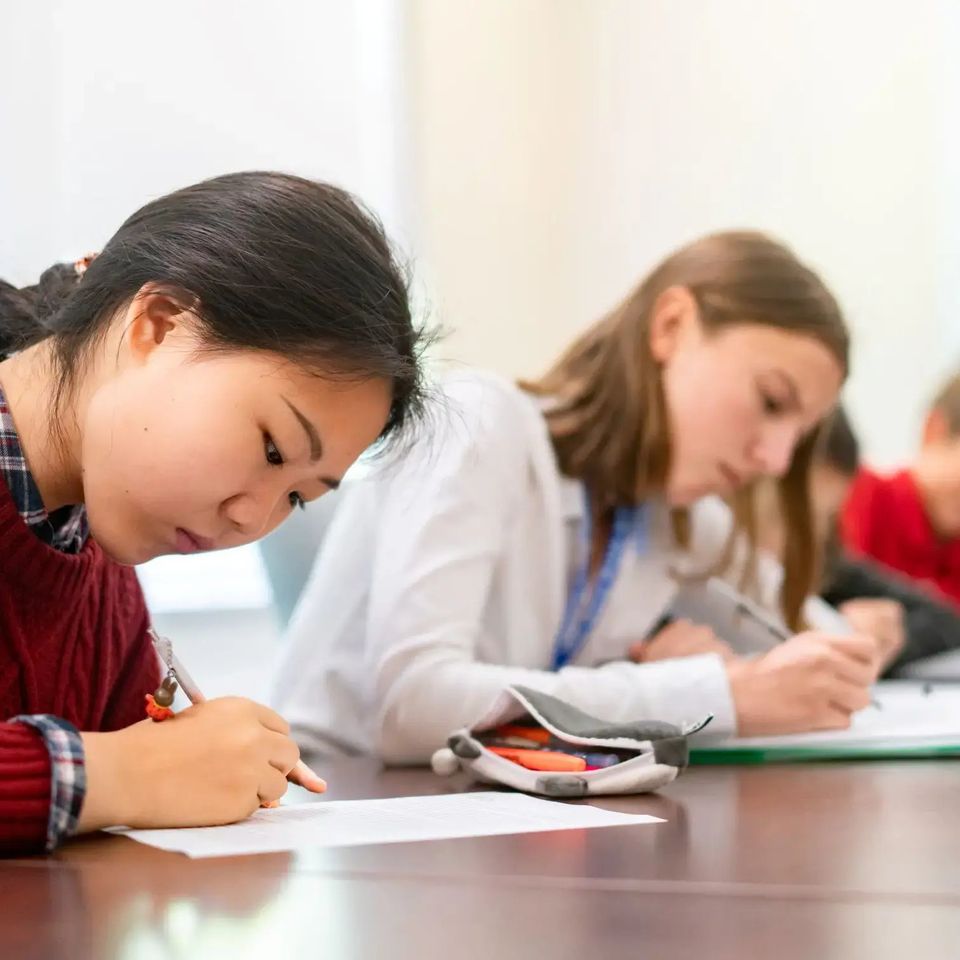 Dois alunos escrevendo em suas carteiras em uma sala de aula
