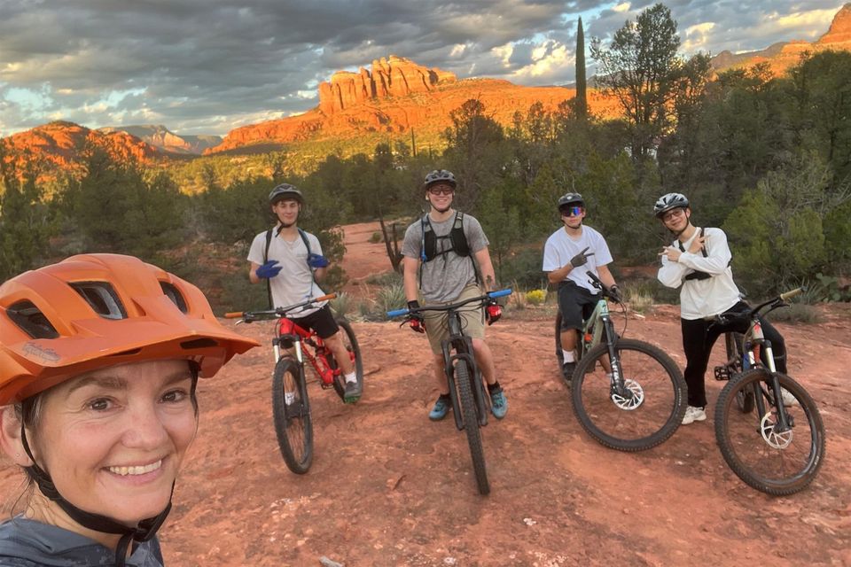 Selfie de grupo de mountain bike: professor e quatro alunos de capacete na rocha, com a Cathedral Rock ao pôr do sol