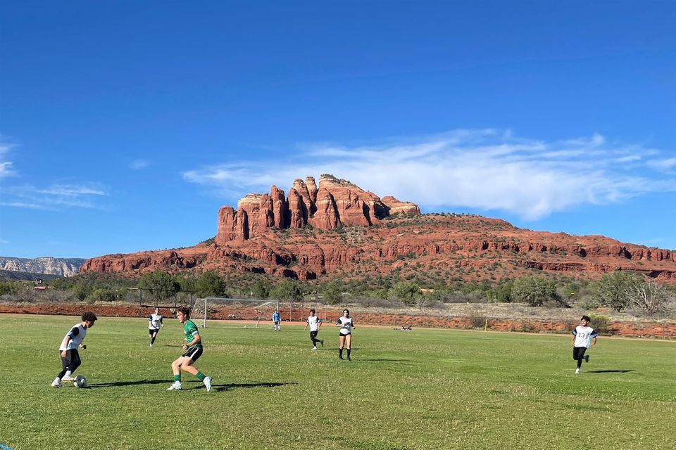 Treino de futebol misto no campo do campus, com a Cathedral Rock e falésias vermelhas ao fundo