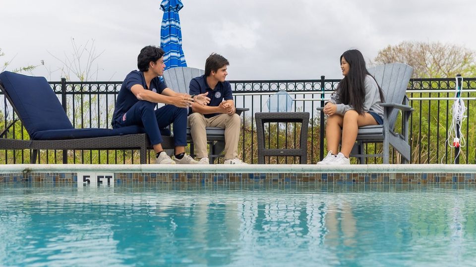 Three uniformed boarding students chatting on loungers beside the boarding village pool
