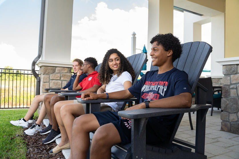 Quatro alunos internos com camisetas da Windermere Prep sentados em cadeiras no pátio do dormitório