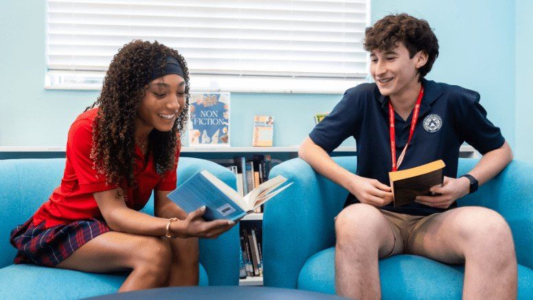 Dois alunos do ensino médio lendo e rindo em poltronas da biblioteca