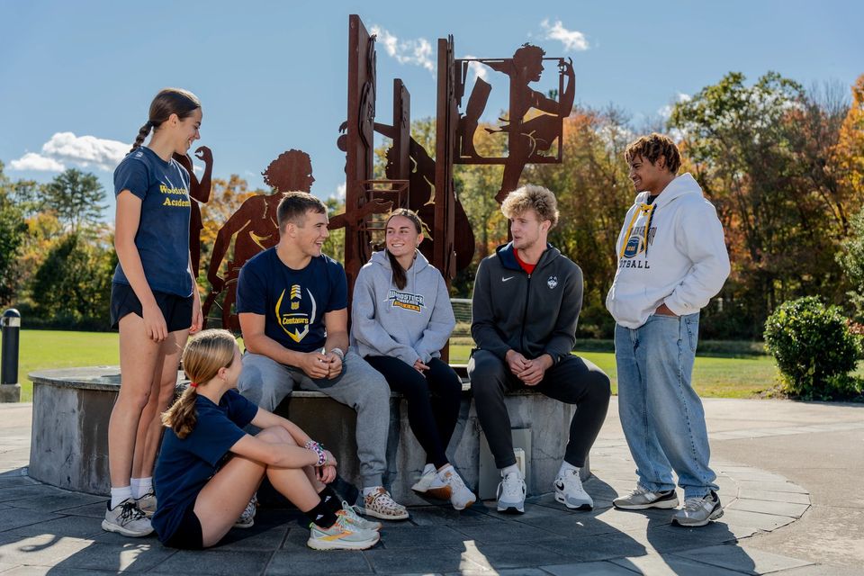 Grupo de alunos com roupas da WA sentados ao redor da escultura do campus ao ar livre