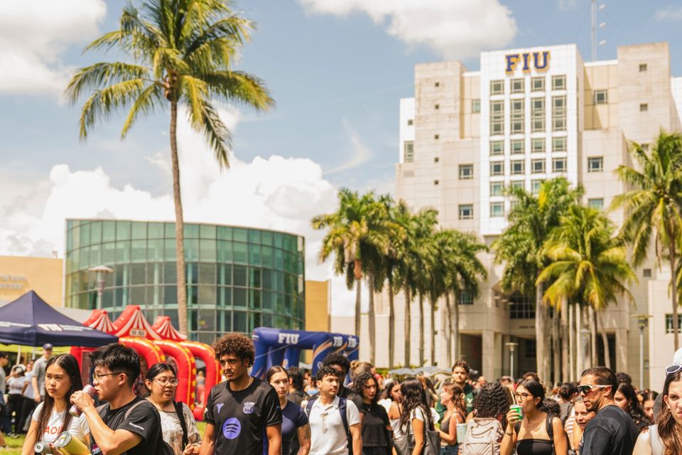 Estudantes reunidos em frente à Green Library, a torre com o letreiro FIU, entre palmeiras no campus Modesto A. Maidique, em Miami