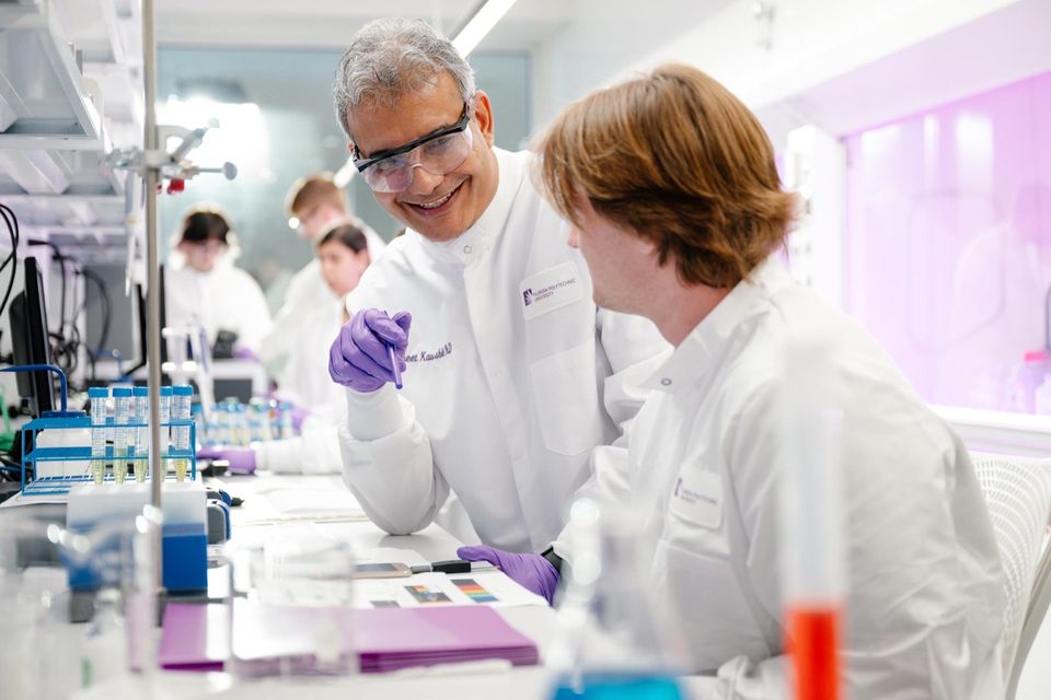 Professor e estudantes de jaleco trabalham em um laboratório da Florida Poly com iluminação roxa