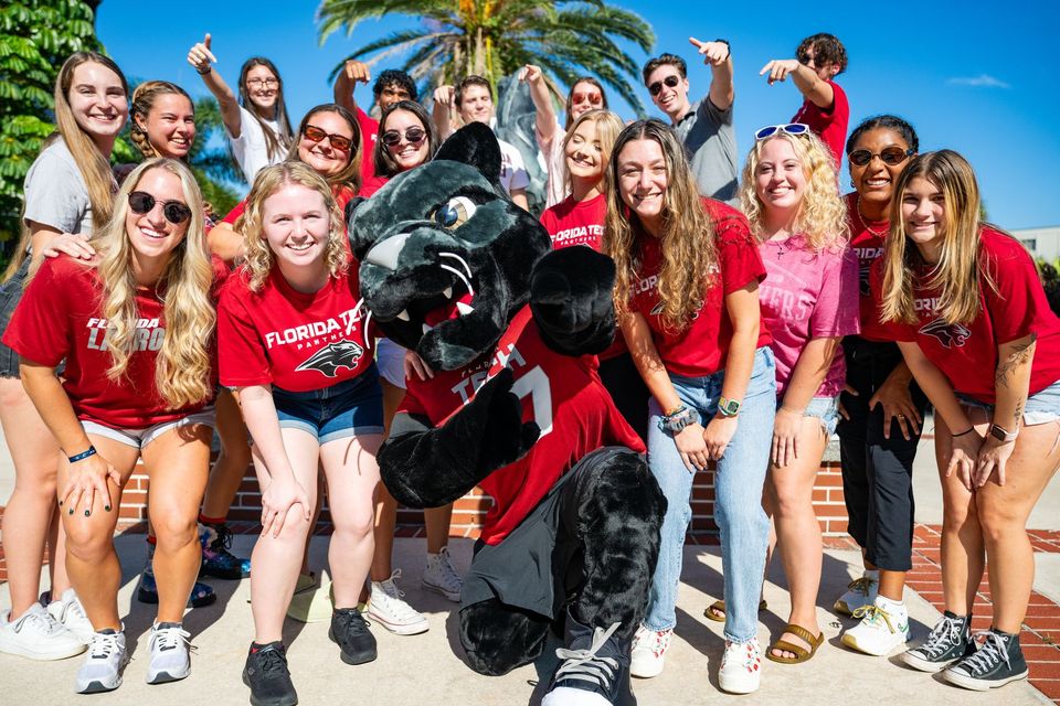 Estudantes com camisetas vermelhas da Florida Tech se divertem ao lado do mascote Pete the Panther